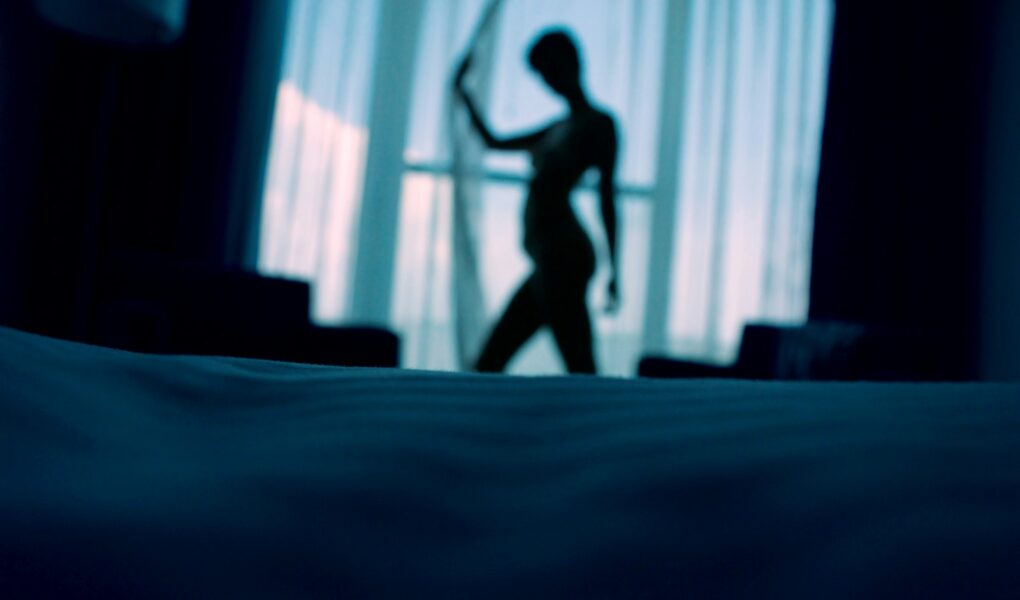 sillouehtte photo of woman standing beside window curtains